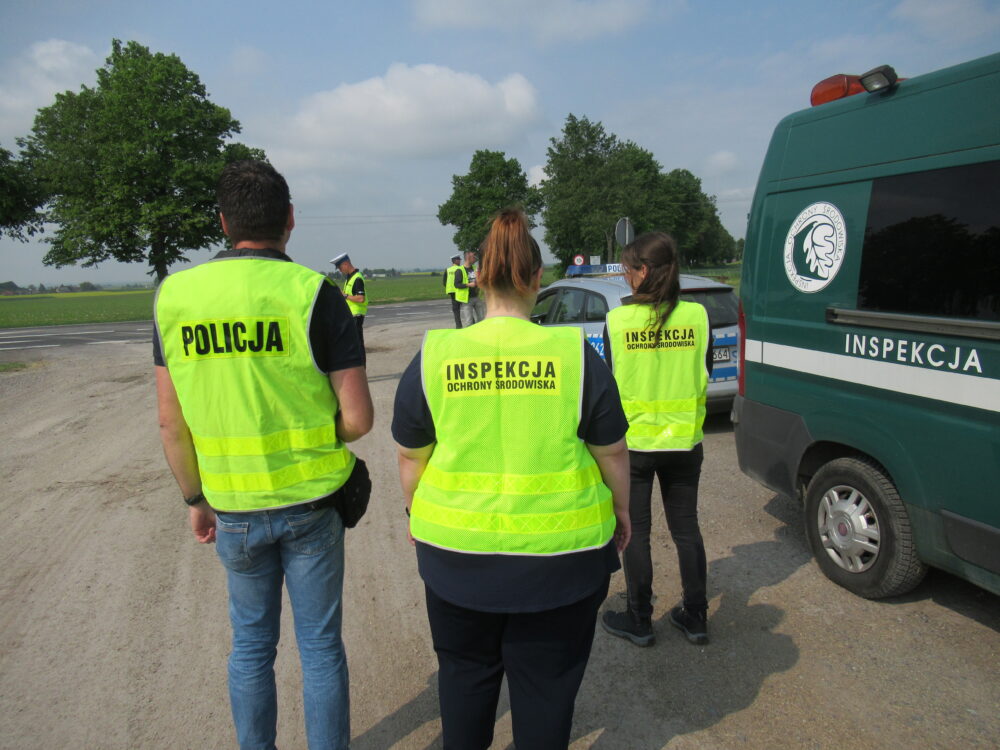 Na pierwszym planie widzimy inspektorów i funkcjonariuszy w jasnych kamizelkach przygotowujących się do kontroli pojazdów przemocnych odpady